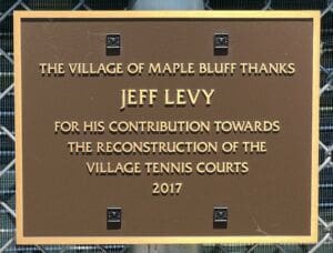 A bronze plaque reads: The Village of Maple Bluff thanks Jeff Levy for his contribution towards the reconstruction of the village tennis courts 2017.