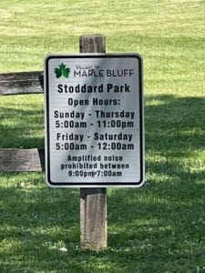 A sign in Maple Bluff’s Stoddard Park displays open hours: Sunday–Thursday 5am–11pm, Friday–Saturday 5am–12am, and states that amplified noise is prohibited from 9pm to 7am.