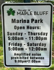 A sign for Village of Maple Bluff Marina Park listing open hours: Sunday-Thursday 5:00am–11:00pm, Friday-Saturday 5:00am–12:00am. Amplified noise is prohibited between 9:00pm–7:00am.